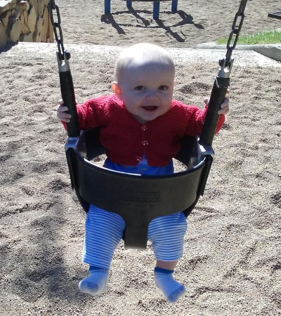 Julian sitting in a baby swing in a knitted red sweater.