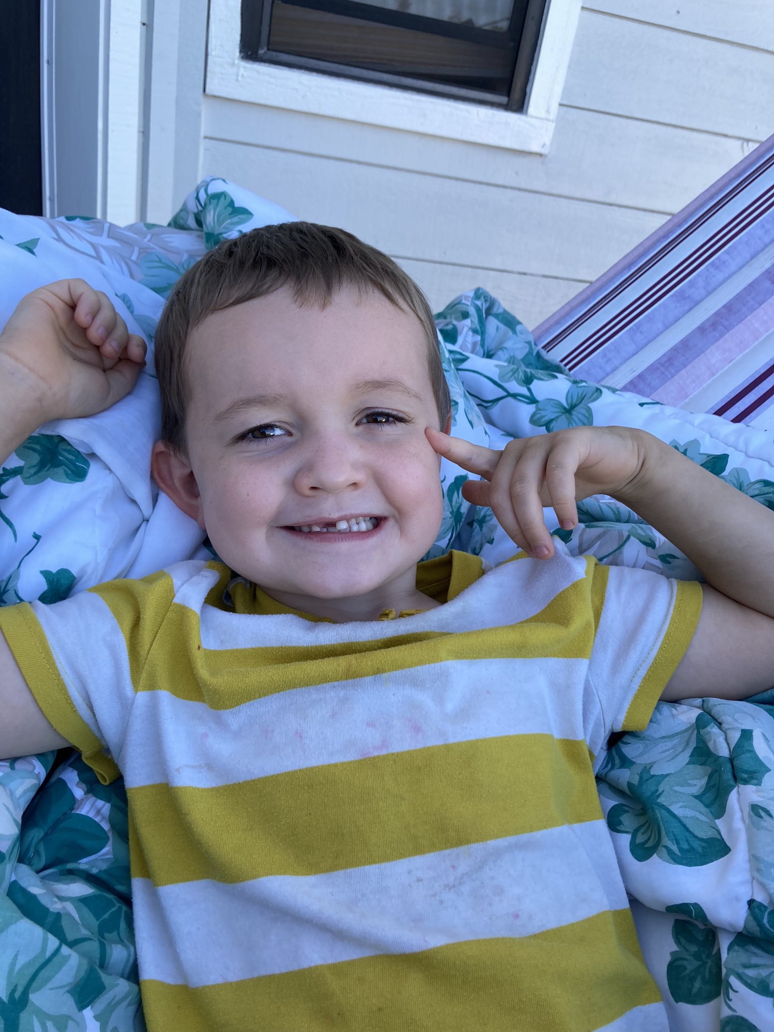 Julian laying outside in the hammock on his blanket with a gap tooth smile.