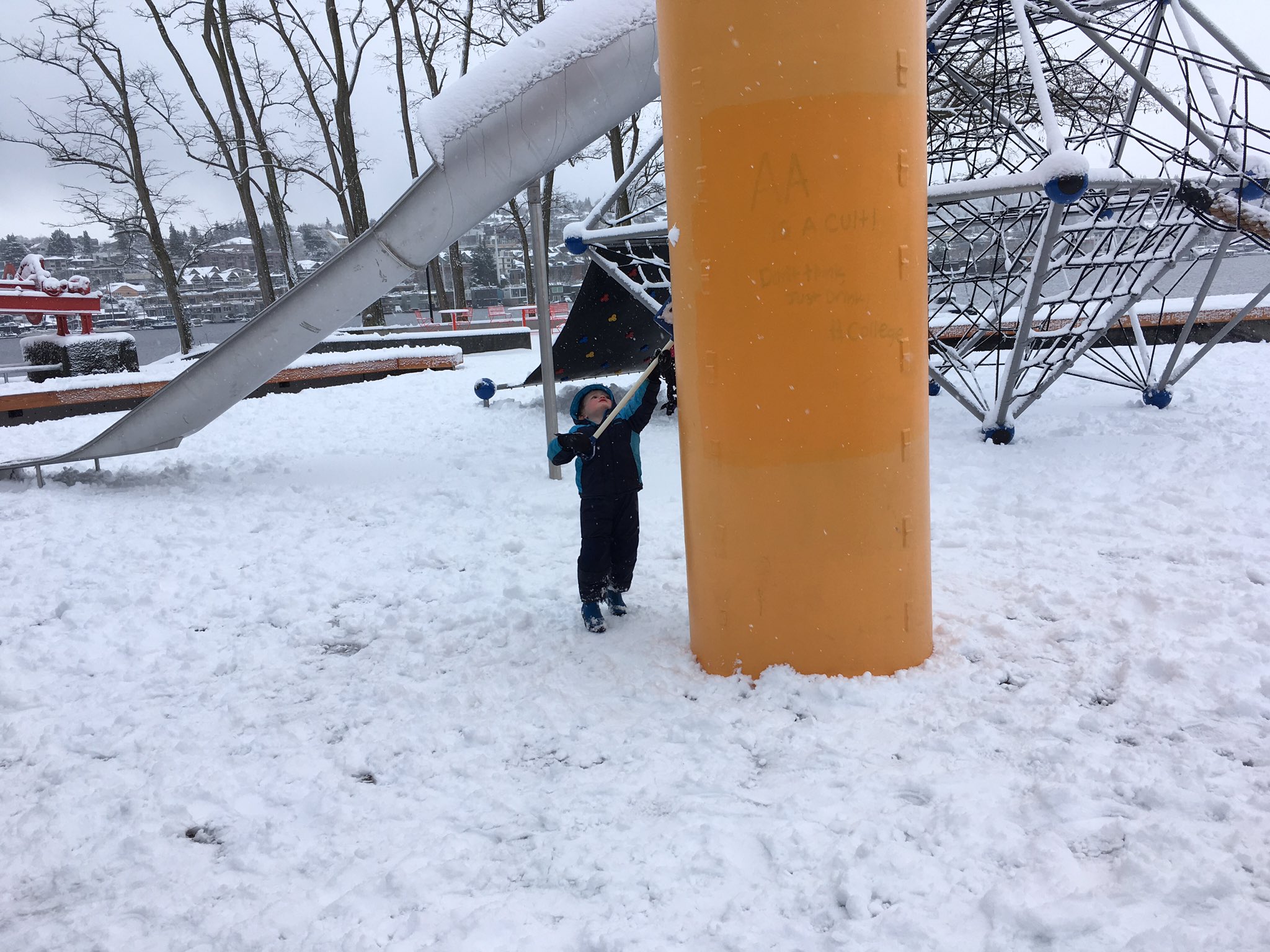 Julian uses a child's plastic snow shovel while partially obscured by a large yellow metal column.