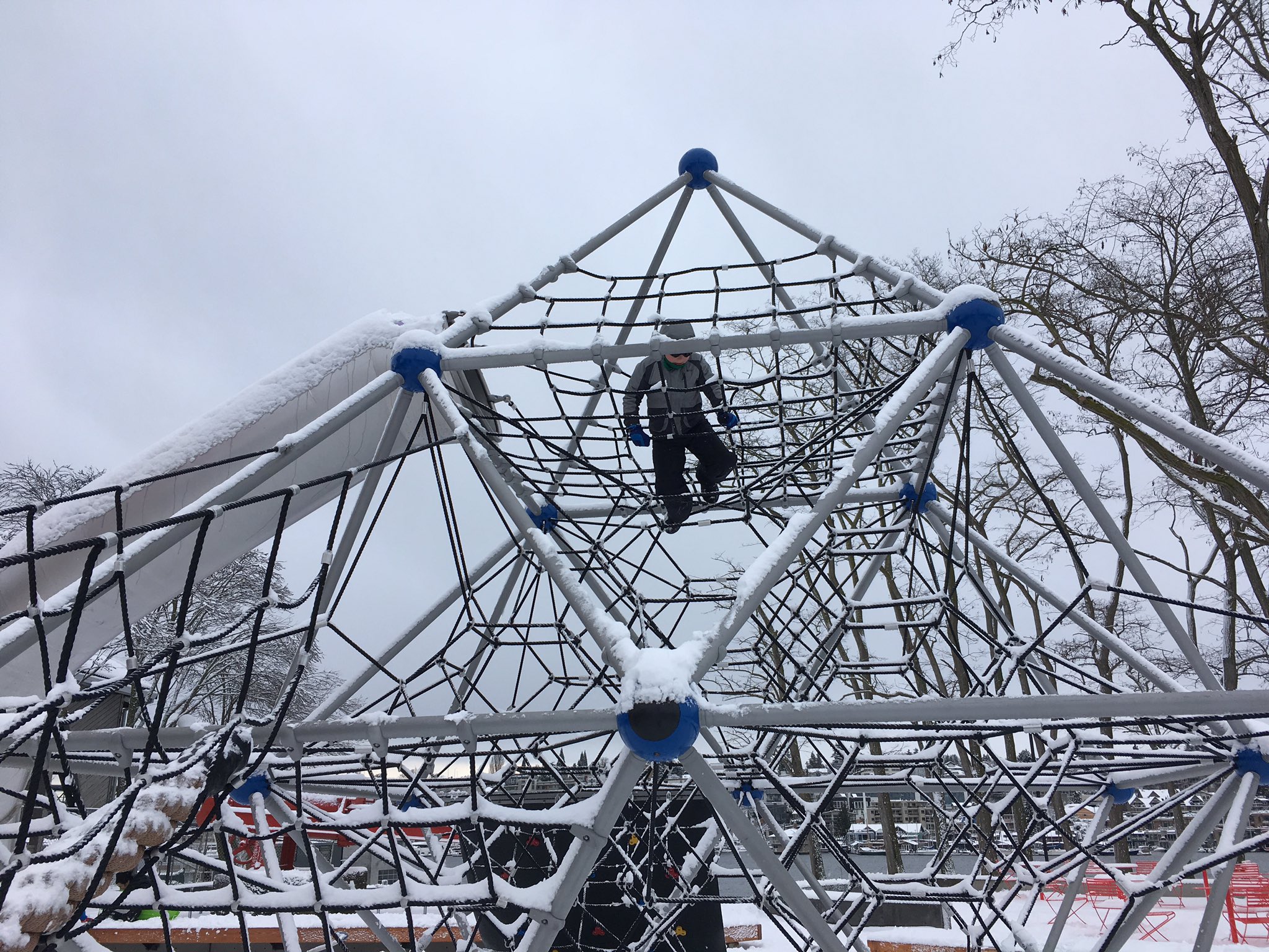 Calvin clambors around a snow covered rope playground dome.