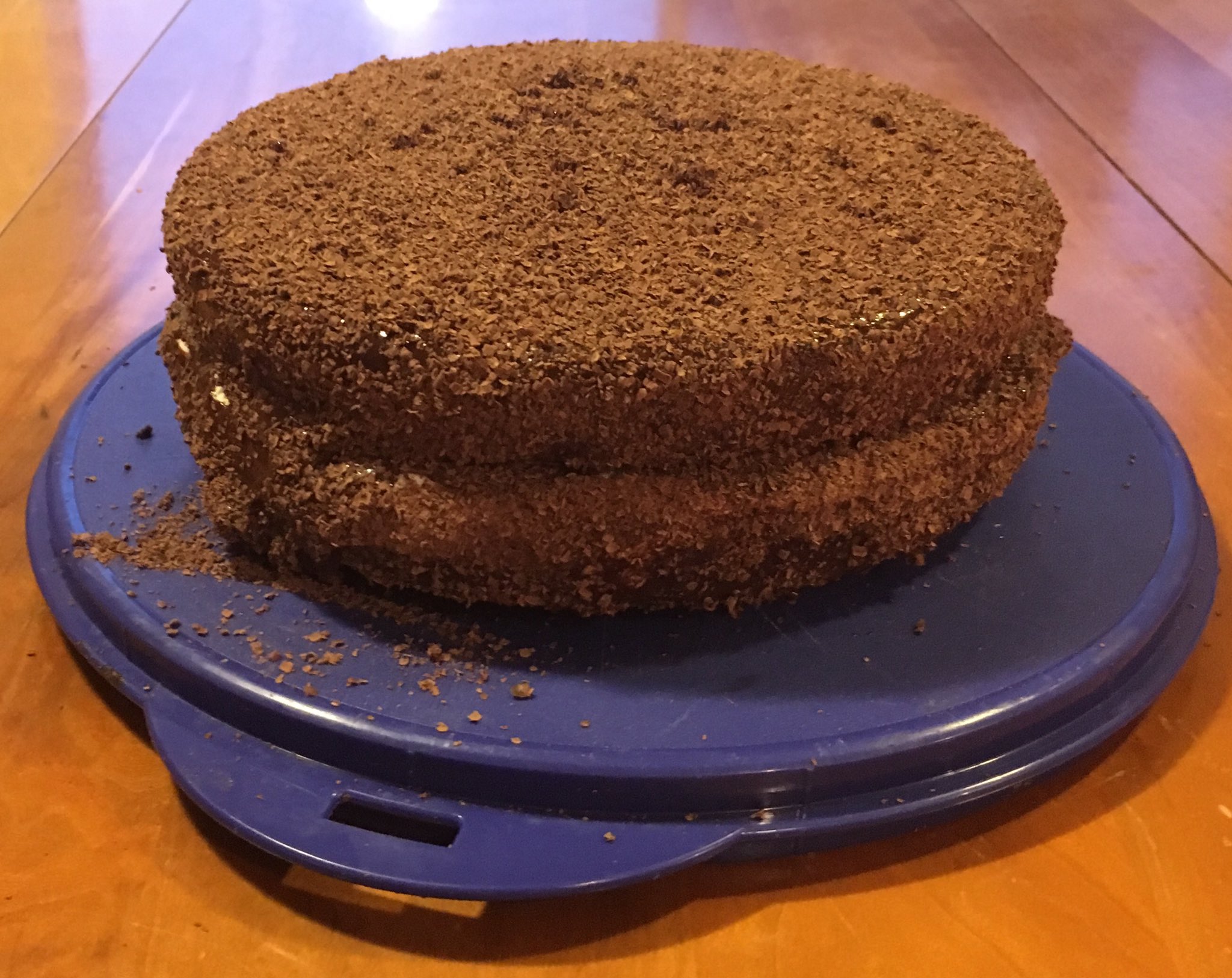 Two layer chocolate cake covered in grated chocolate sitting on a plastic blue cake platter.