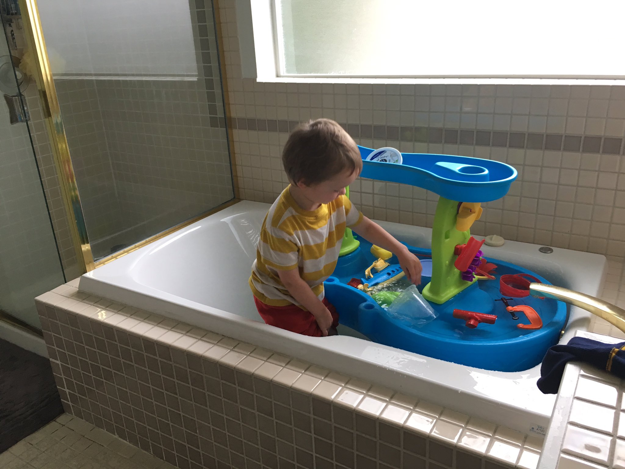 Julian standing in a large master bathtub playing with a blue water table, also in the bathtub.