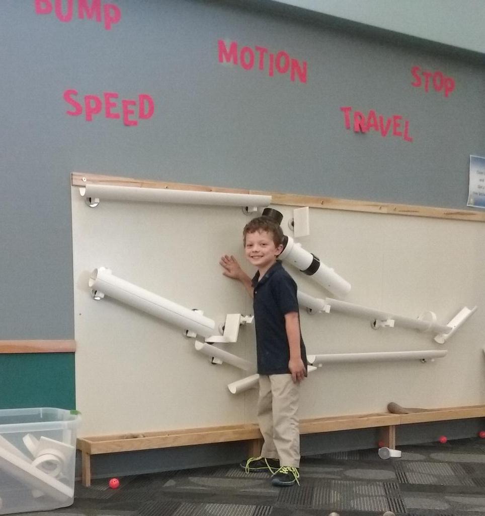 Calvin standing in front of a board with tubes that can be rearranged and allow balls to roll down in various configurations.