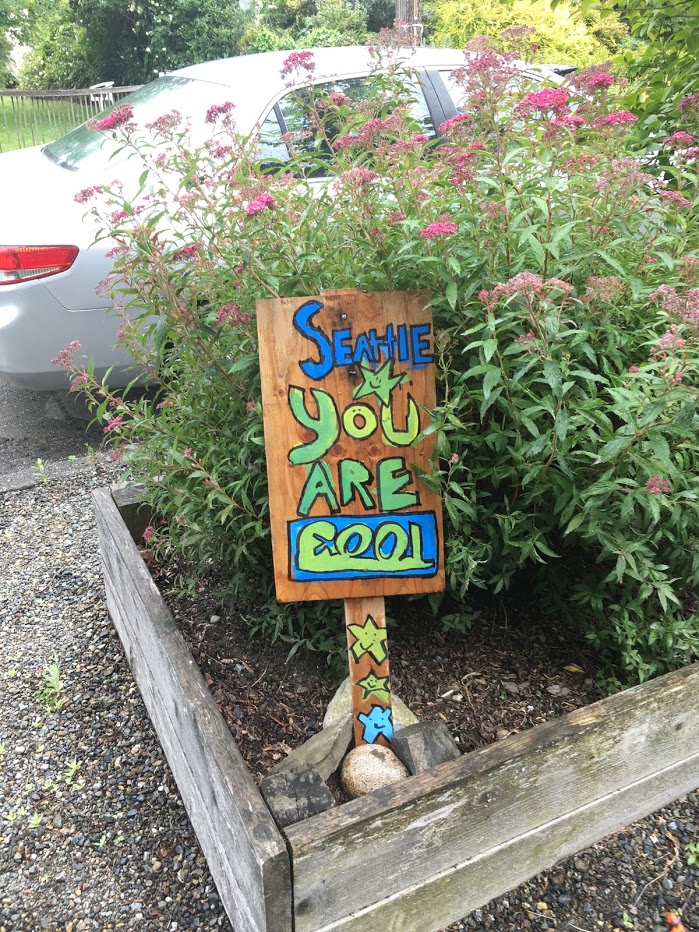 Wooden sign with words in blue and green that says "Seattle You Are Cool".