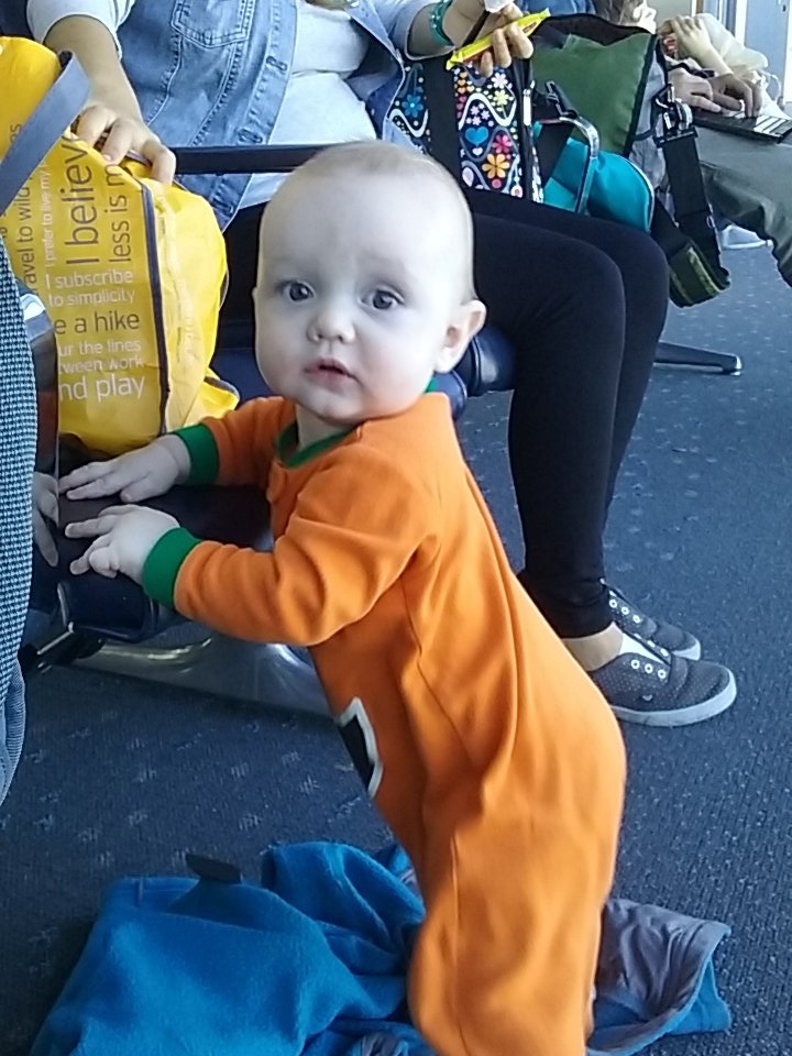 Baby Julian stands up by bracing his hands against the airport seats.