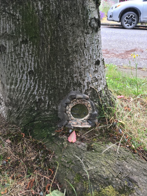 Round fairy door, surrounded by cobble stone, in tree trunk.