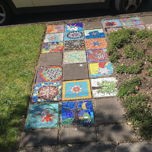 Twenty-two 12-inch mosaics with various pictures on them used to create a sidewalk path.