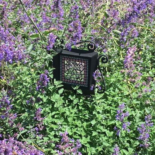 Mosaic mirror made with reflective mosaic tiles in the middle of purple flowers.