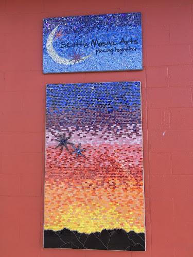 Two mosaics on red wall. Top mosaic shows a crescent moon and says Seattle Mosaic Arts piecing together. Bottom mosaic shows a sunset.