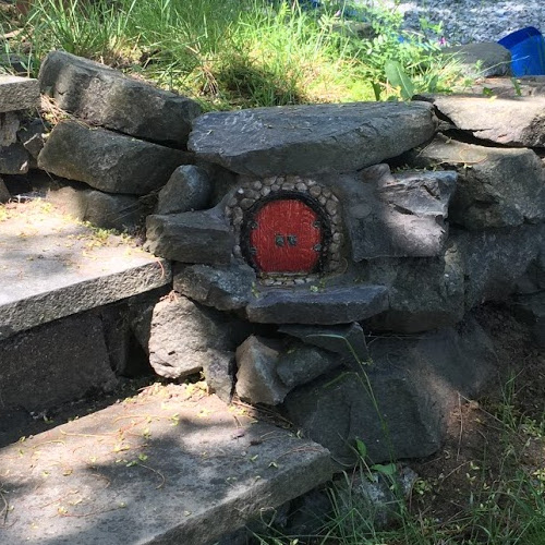 Red round fairy door embedded in stones next to stairs.