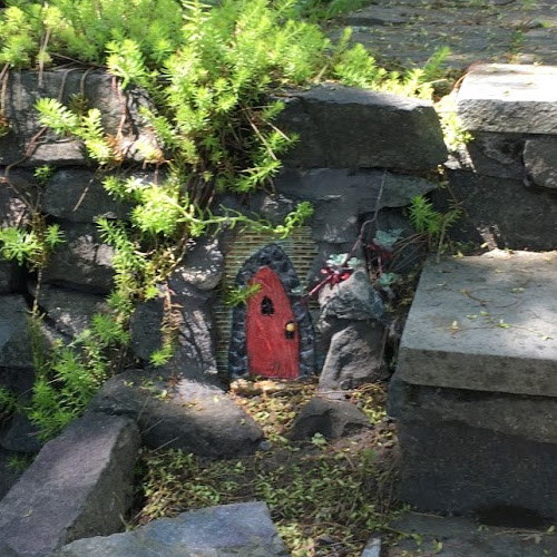 Gothic-style red fairy door embedded in stone next to stairs.