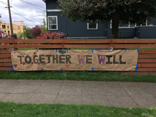 Sign on fence says "Together We Will" with smaller, hard to read, writing around the bigger letters.